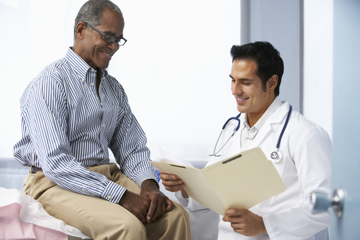 Doctor In Surgery With Male Patient Reading Notes Looking Happy.